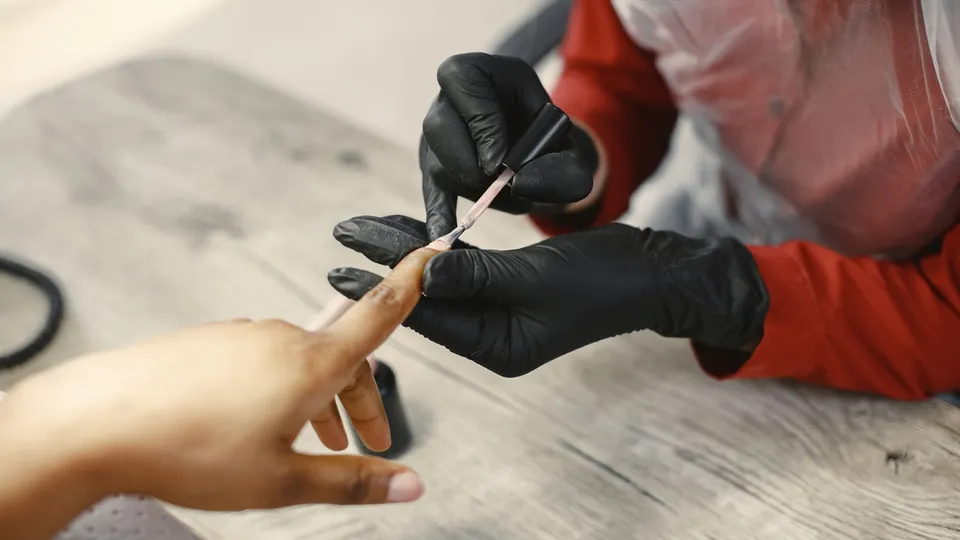 戴黑色手套的美甲师在木桌上为顾客涂裸色指甲油