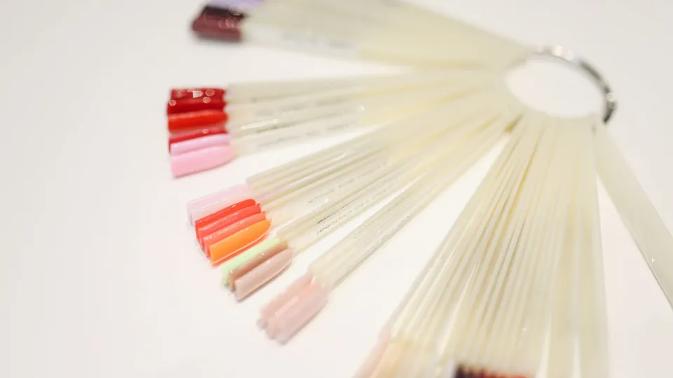 A fan of nail colour sample tips in reds, pinks and oranges on a white table